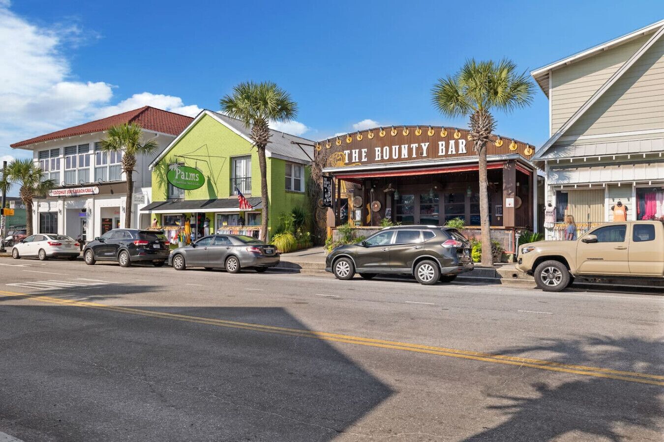 A street view with a green building labeled "Palms" and a bar named "The Bounty Bar" with palm trees in front.