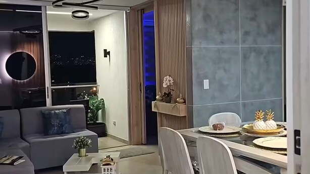 A modern living room with a gray sofa, a dining table with white chairs, and a large window overlooking a cityscape at night. - Beautiful apartment with a spectacular view (Cali)