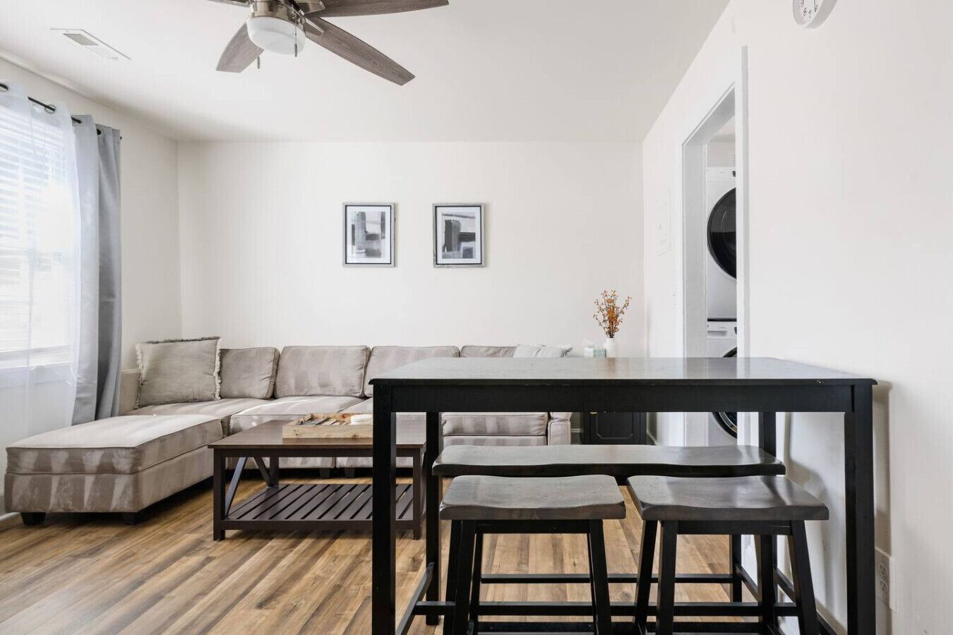 Un salon moderne avec un canapé, une table à manger avec des bancs, un ventilateur de plafond et deux tableaux encadrés accrochés au mur.