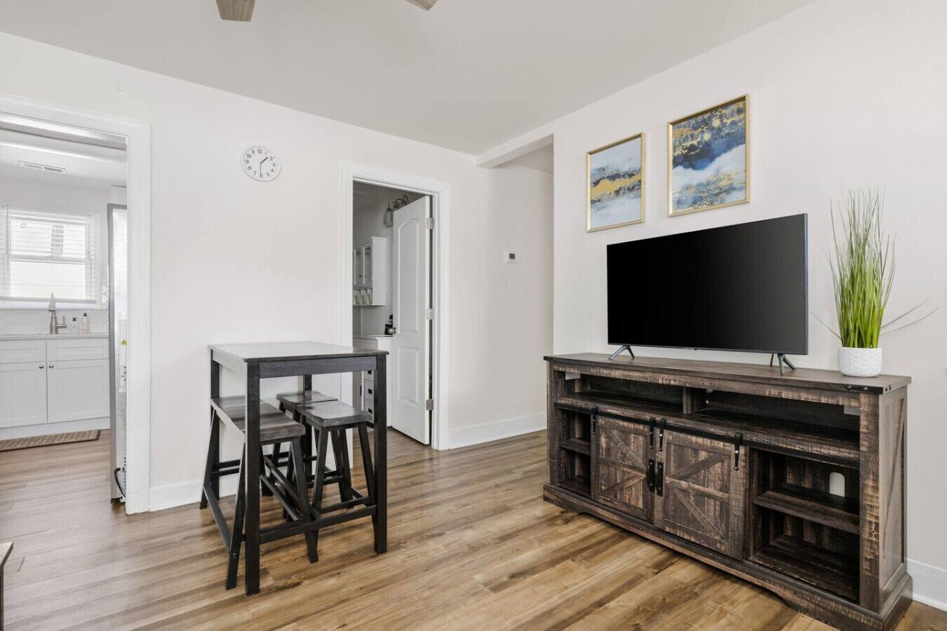 Un salon moderne avec un plancher en bois, une table à manger avec des chaises, un téléviseur posé sur un meuble en bois et deux tableaux encadrés accrochés au mur.