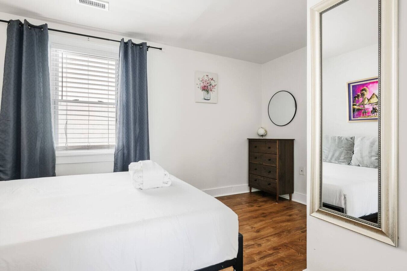 A bedroom with a bed, a dresser, a mirror, and a window with curtains.