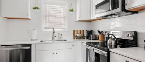 Una cocina moderna con armarios blancos, lavavajillas de acero inoxidable, horno empotrado y microondas.