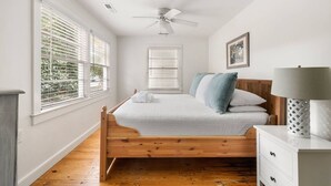 A bedroom with a wooden bed, white walls, and a ceiling fan. - Beach Maverick - 3 BR 2 Bath 1 Block to Center St! (Folly Beach)