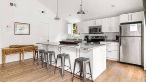 A modern kitchen with white cabinets, stainless steel appliances, and a central island with stools. - Beach Maverick - 3 BR 2 Bath 1 Block to Center St! (Folly Beach)