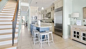 A modern kitchen with a central island, stainless steel appliances, and a staircase with wooden railings. - 4 Bedroom Oceanfront Condo with Rooftop-Walkable-B (Folly Beach)