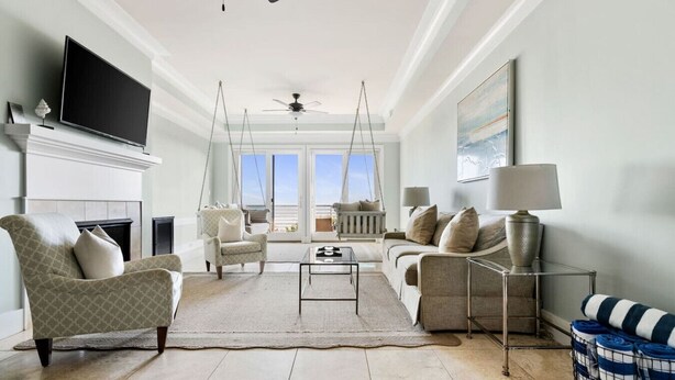 A spacious living room with a fireplace, a television, a swing chair, a sofa, and a view of the outdoors. - 4 Bedroom Oceanfront Condo with Rooftop-Walkable-B (Folly Beach)
