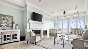 A spacious living room with a fireplace, a television, and a view of the ocean through large windows. - 4 Bedroom Oceanfront Condo with Rooftop-Walkable-B (Folly Beach)
