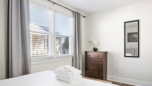 Ein Schlafzimmer mit einem Bett, einem Schminktisch, einem Fenster mit Jalousien und einem Spiegel an der Wand.