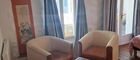 Una habitación con dos sillones, una mesita de madera, una bandeja roja y una puerta que da al exterior.