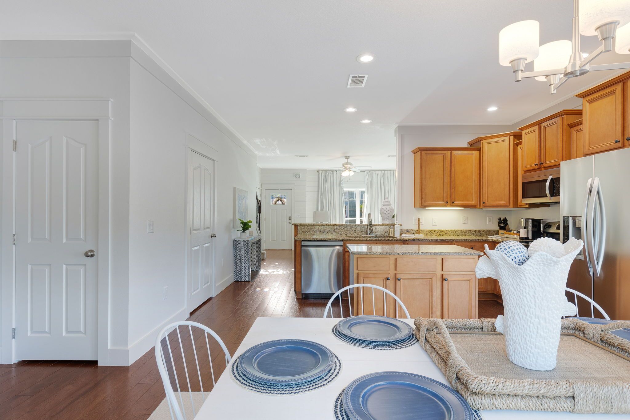 A modern kitchen with wooden cabinets, stainless steel appliances, and a dining area with a white table and blue plates.