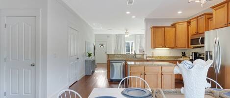 A modern kitchen with wooden cabinets, stainless steel appliances, and a dining area with a white table and blue plates.