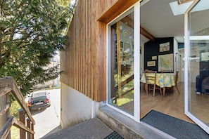 Pared exterior de madera, puerta de vidrio que da a un área interior con mesas y sillas, y un coche estacionado afuera.