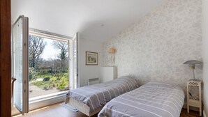 Une chambre avec deux lits, une fenêtre donnant sur des arbres, un radiateur et une table de chevet avec une lampe.