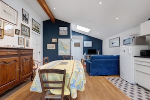 Un comedor con una mesa preparada para cuatro personas, un sofá azul, una cocina con microondas y refrigerador, y un armario de madera.