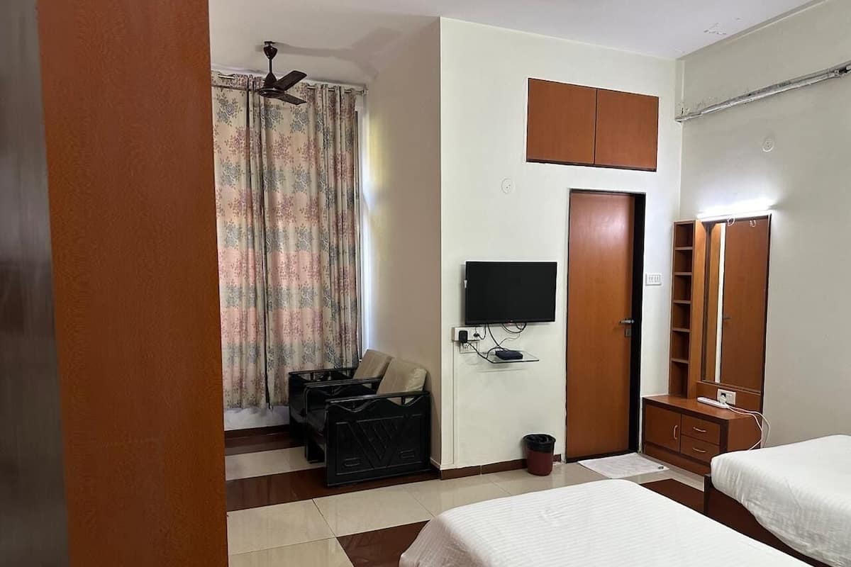 Ein Hotelzimmer mit zwei Betten, einem Fernseher, einem Kleiderschrank und einem Schreibtisch mit Stuhl.