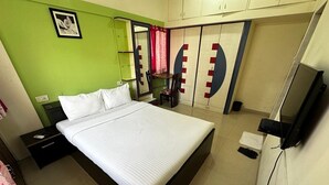 A bedroom with a bed, a nightstand, a chair, a wardrobe, and a television. - Amicable Corporate Apartment (Mumbai)