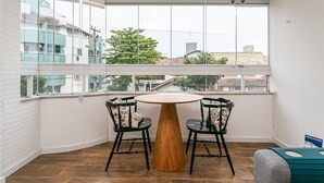 Una stanza angolare con un tavolo rotondo in legno e due sedie, ampie finestre vista sulla città e pavimento piastrellato.