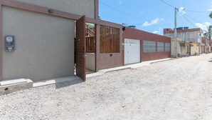Une rue résidentielle bordée de maisons, avec une entrée sécurisée par un portail et un coffret électrique sur le trottoir.