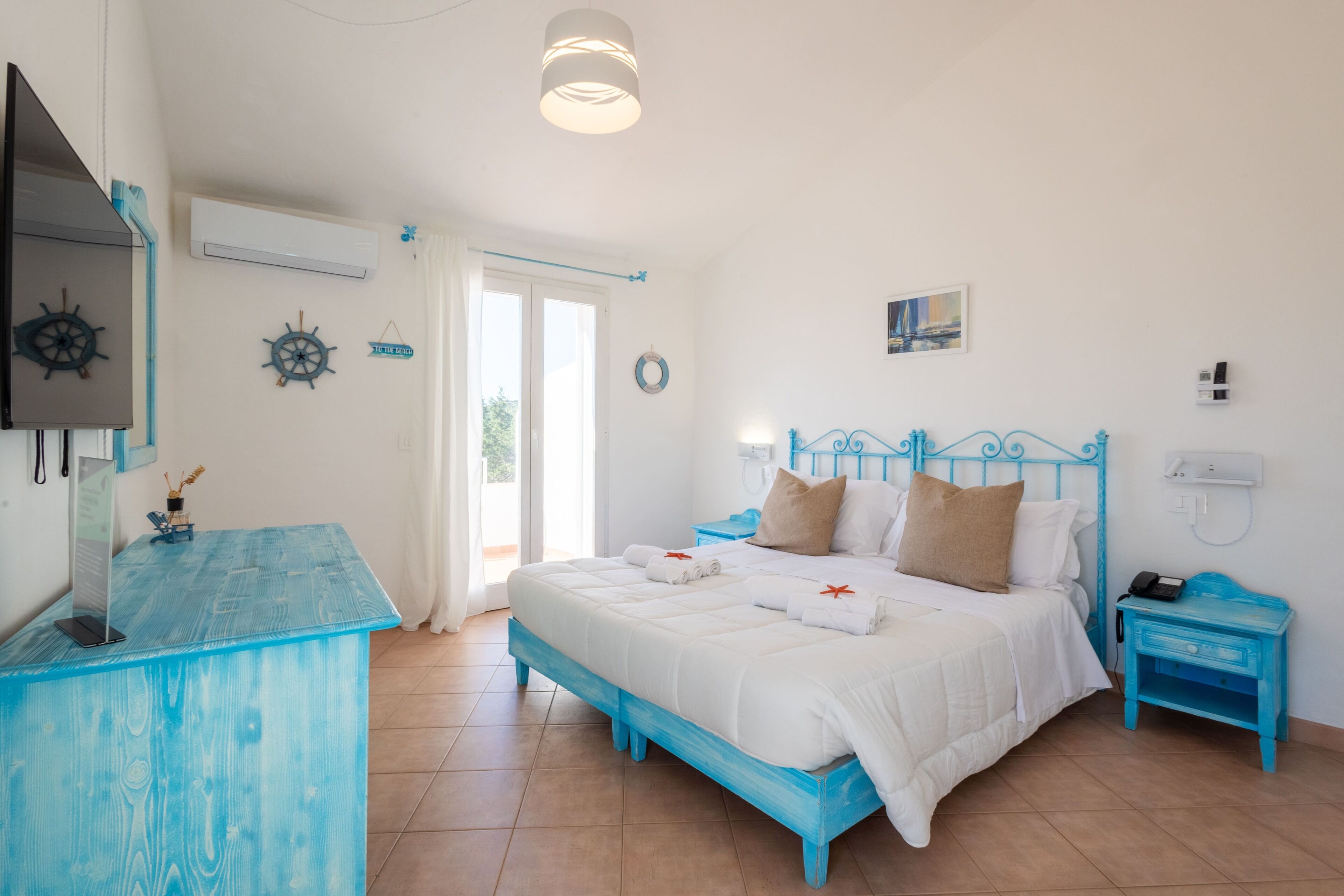 Quarto com cama, escrivaninha, cadeira, mesa de cabeceira e TV fixada na parede.