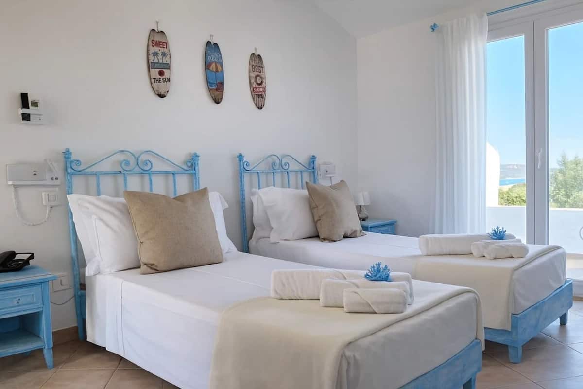 A hotel room with two beds, a small desk, and a view of the sea.