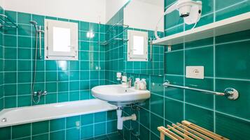 A bathroom with a white bathtub, a sink, a mirror, and a shower.