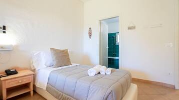 A bedroom with a bed, a nightstand with a phone, and a bathroom visible through an open door.