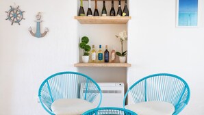 A room with two blue wicker chairs, a small round table, a wooden wine rack with bottles, and a white wall with a framed picture. - Hotiday Baja Sardinia Seaside (Baja Sardinia)