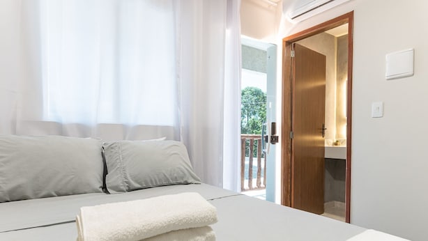 Un dormitorio con cama, cortinas blancas, una puerta de madera y vistas a un balcón.
