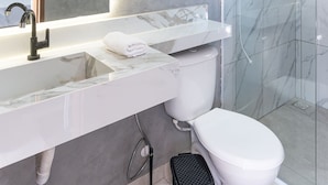 Un baño moderno con un espejo grande, un lavabo blanco, un inodoro y una cabina de ducha de vidrio.