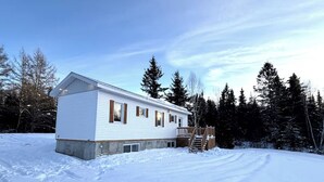 Une petite maison blanche d’un seul étage, dotée d’une terrasse en bois et d’un escalier menant à l’entrée.