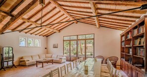 A spacious room with a high wooden ceiling, a long dining table, a sofa, and a bookshelf. - Hotiday Grosseto Podere (Grosseto)