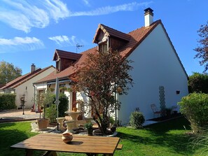 A two-story house with a sloped roof, a garden with potted plants, and a wooden table in the foreground. - Bed and Breakfast. Pets allowed. (Marcilly-en-Villette)