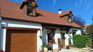 A two-story house with a brown tiled roof, a wooden garage door, and a front garden with potted plants and a gravel pathway. - Bed and breakfast. Pets allowed. (Marcilly-en-Villette)