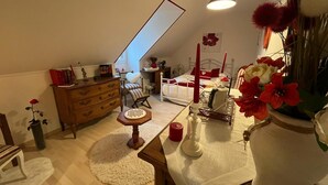 A cozy attic bedroom with a sloped ceiling, a wooden dresser, a chair, a bed with red accents, and a vase with red flowers. - Bed and breakfast. Pets allowed. (Marcilly-en-Villette)