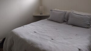 Een slaapkamer met een bed, kussens, een nachtkastje, een lamp en een raam.