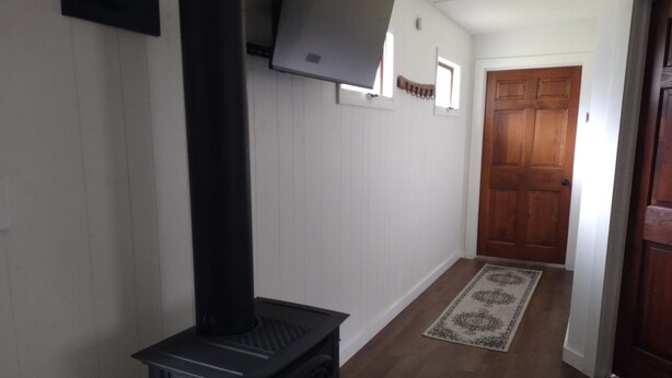 Een kamer met een zwarte houtkachel, witte lambrisering, een houten deur en een kamerbreed tapijt op de vloer.