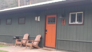 Een gebouw met een groene gevel, een rode deur en twee Adirondack stoelen ervoor.