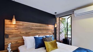 Een moderne slaapkamer met een houten hoofdbord, een groot bed met meerdere kussens, een nachtkastje en een potplant.