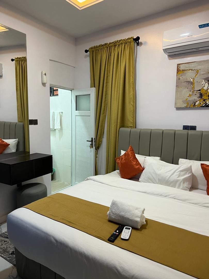A hotel room with a bed, a bedside table, a mirror, a door, and an air conditioning unit.