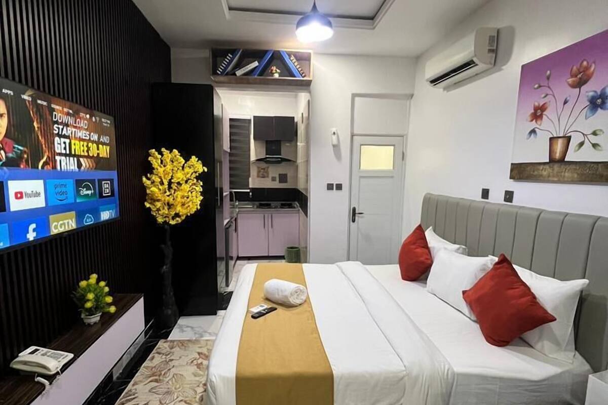 A modern hotel room with a bed, a TV, a desk, and a bathroom visible through an open door.
