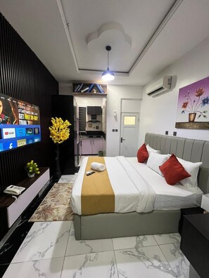 Une chambre d’hôtel moderne équipée d’un lit, d’une télévision, d’un bureau et d’une salle de bain visible à travers une porte ouverte.