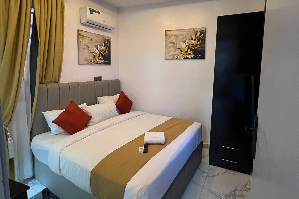 A modern hotel room with a bed, air conditioning unit, artwork, and a wardrobe.
