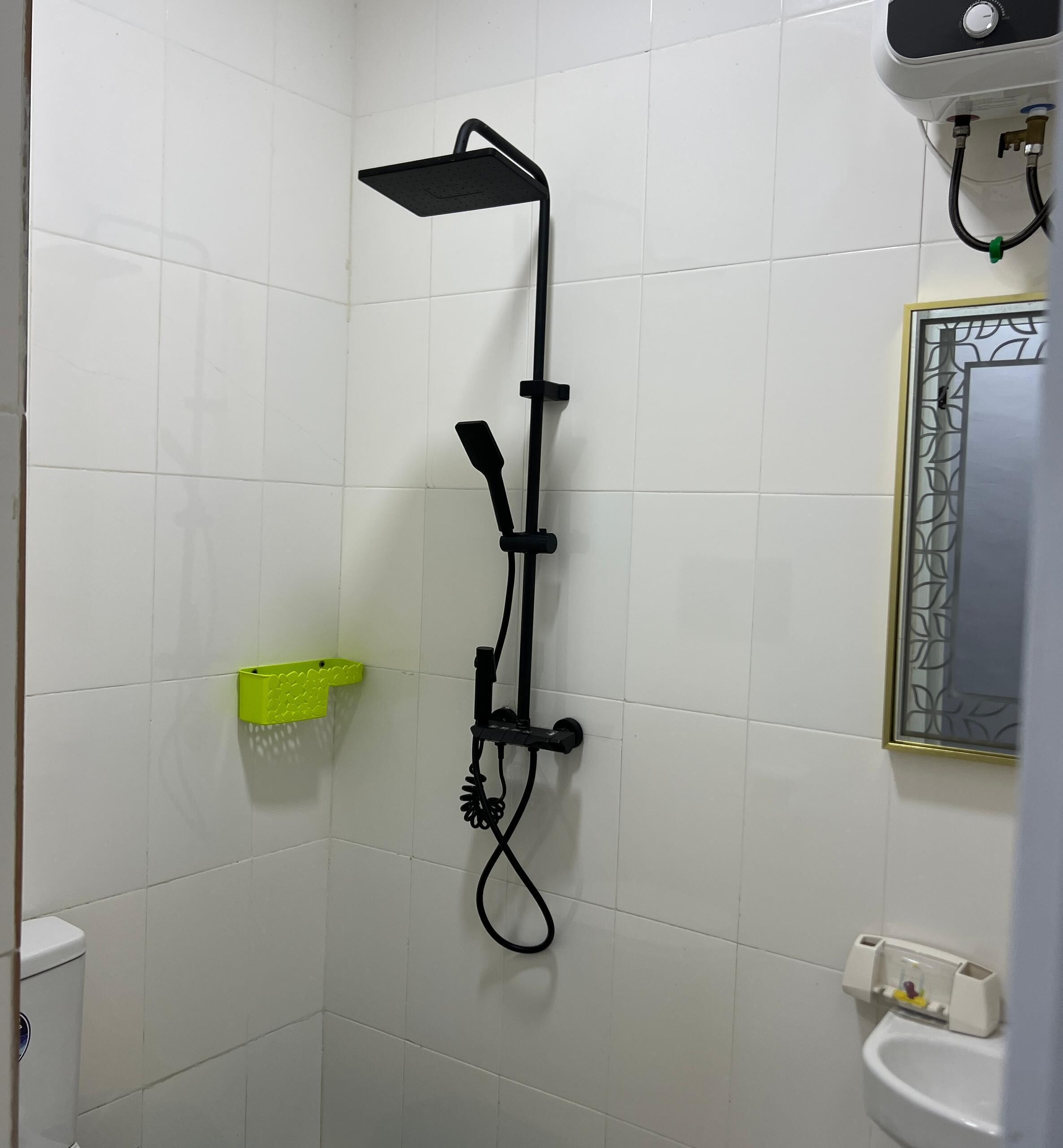 A shower with a handheld showerhead, a wall-mounted faucet, and a green soap dish.