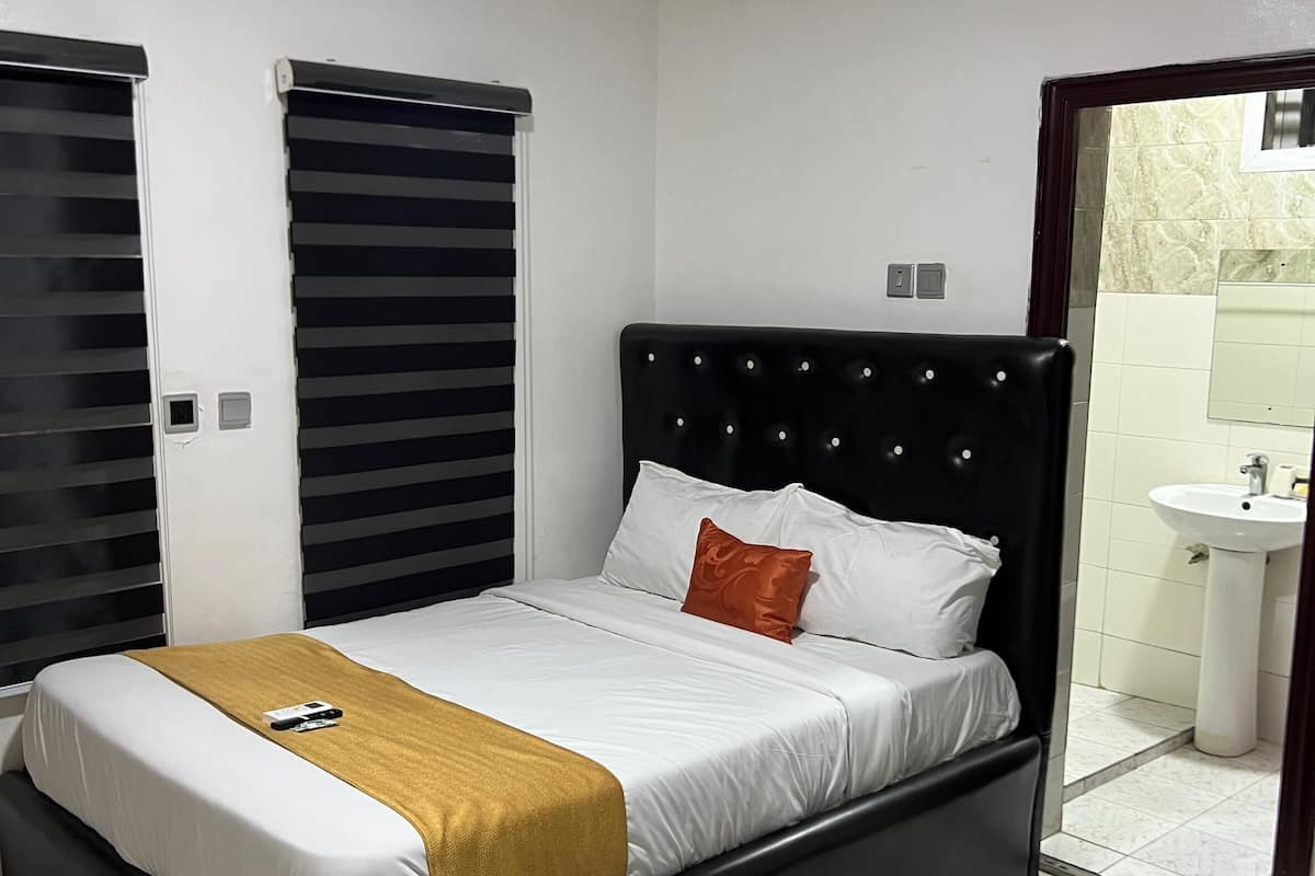 A bedroom with a black bed frame, white bedding, and a mustard-colored throw blanket.