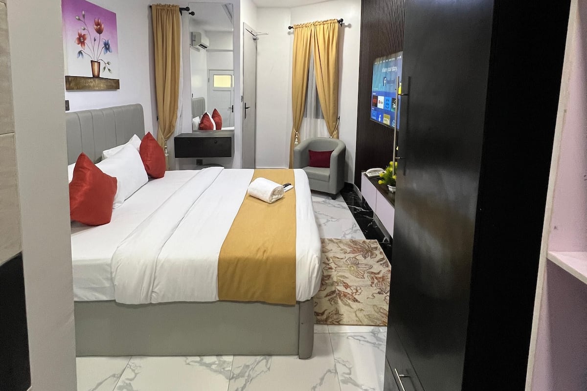 A modern hotel room with a large bed, a flat-screen TV, a desk with a chair, and a wardrobe.