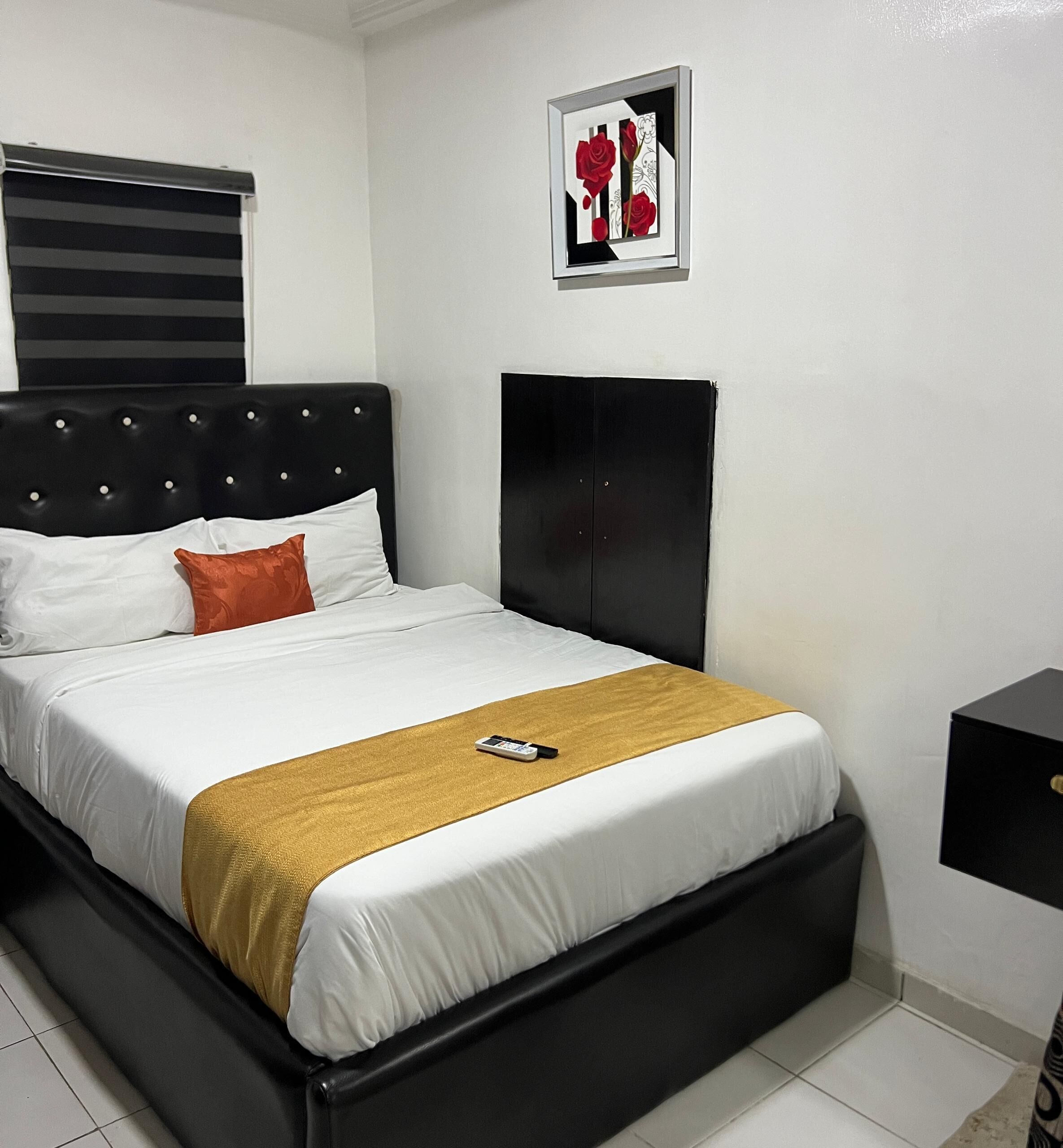 A neatly made bed with a white and gold bedspread, a black headboard, and a single red pillow.