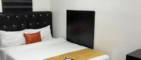 A neatly made bed with a white and gold bedspread, a black headboard, and a single red pillow.