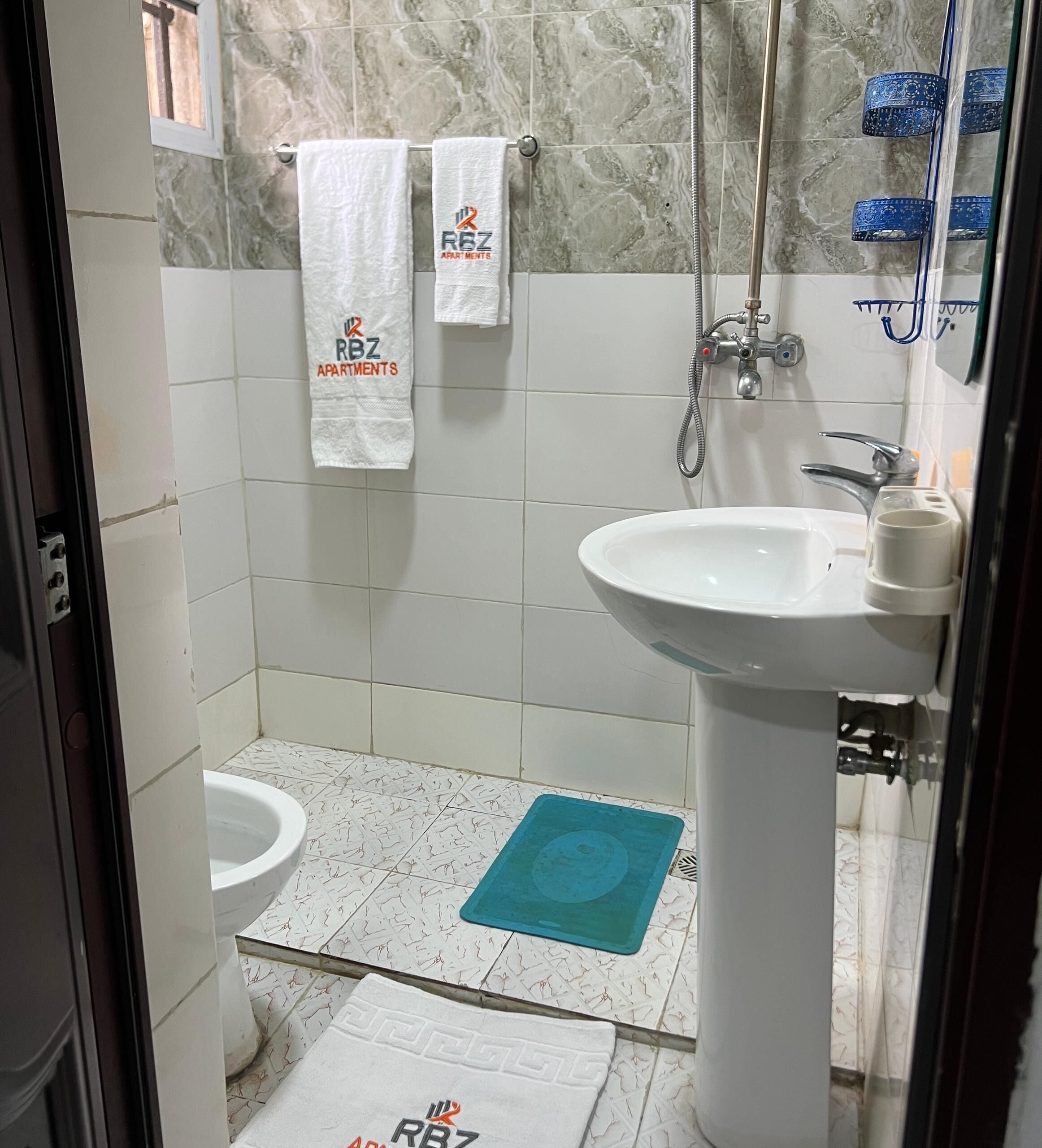 A bathroom with a white sink, a shower, and a toilet. There are towels hanging on a rack and a blue mat on the floor.