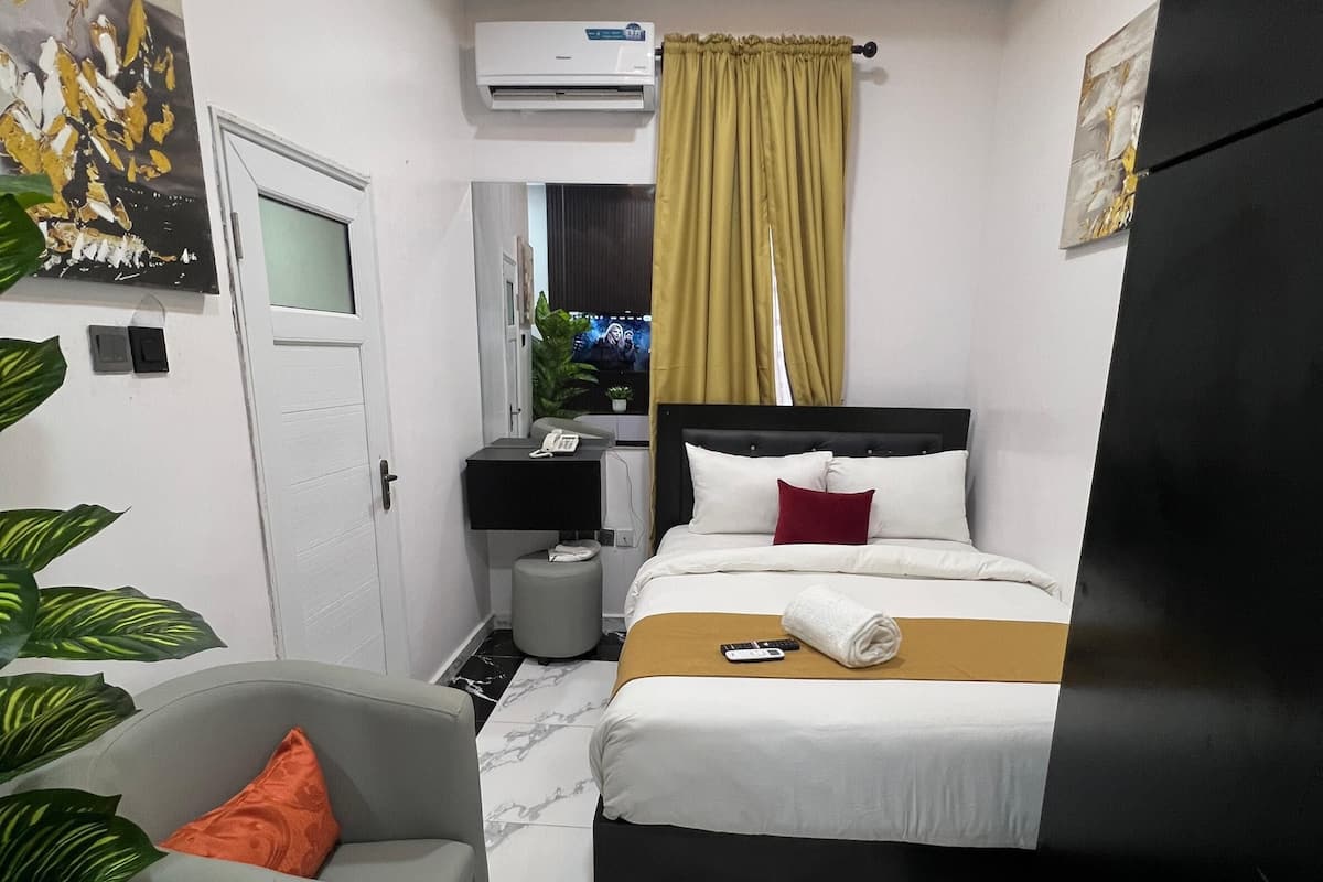 A hotel room with a bed, a desk, a chair, a TV, and a wardrobe.