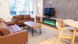 A modern living room with a leather sofa, a wooden coffee table, a TV mounted on a wall, and a fireplace. - Pristine Brand New Duplex, Prime Location! (Vancouver)